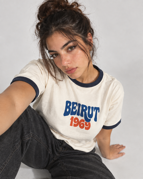 Model wearing a cream Monani ringer T-shirt with blue and orange Beirut 1969 lettering