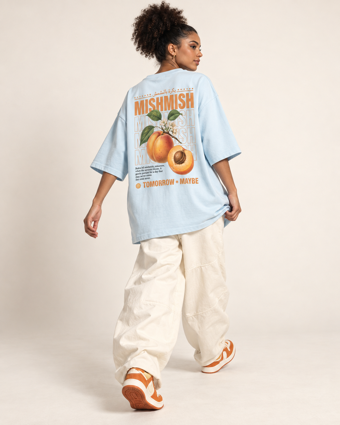 Model wearing a light blue Monani Mishmish T-shirt with an apricot graphic on the back