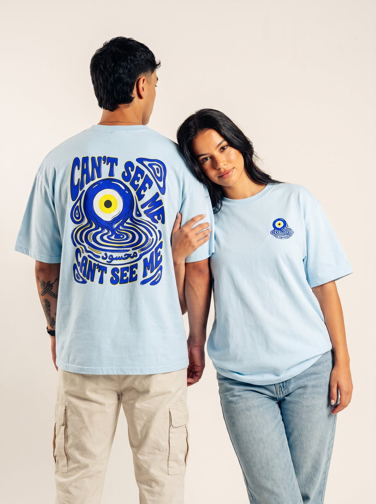Two models showing the front and blue evil eye back graphic on a light blue Monani Mahsood T-shirt